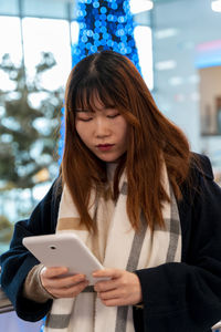 Young pretty woman of chinese ethnicity while typing a tablet in front of blue christmas tree indoor