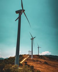 Low angle view of windmills on field against sky