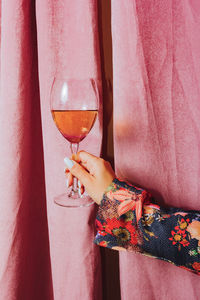 Female hand holding glass of wine. pink curtain in the background.