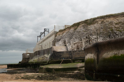 Concrete wall by beach against cloudy sky