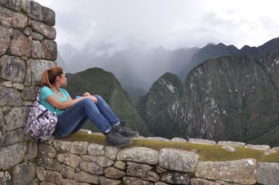 Side view of woman sitting on rock against sky