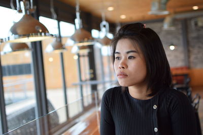 Thoughtful beautiful young woman looking away while sitting in cafe
