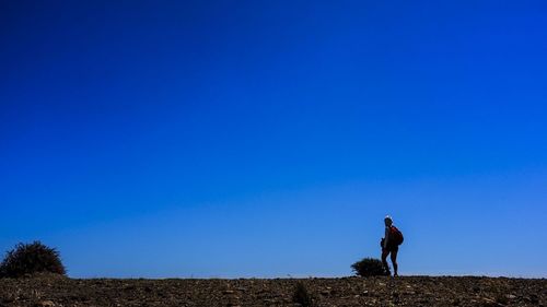 Man standing on field against clear blue sky