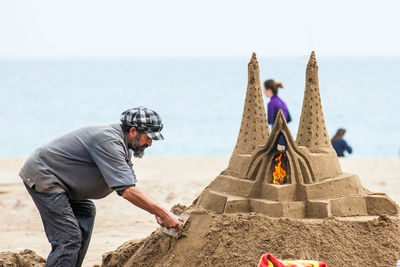 Rear view of men on rock at beach against sky