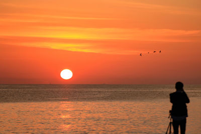 Silhouette woman standing on beach against orange sky