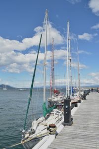 Sailboats moored at harbor against sky