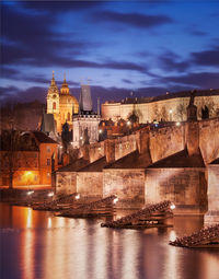 Illuminated buildings by river against sky at night