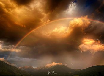 Scenic view of rainbow over mountains against dramatic sky