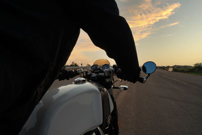 Man riding motorcycle on street against sky during sunset