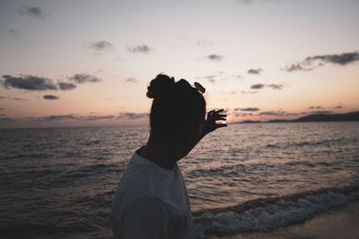 Optical illusion on young woman holding sun at beach against sky during sunset