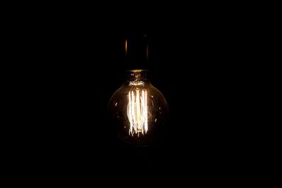 Close-up of illuminated light bulb over black background