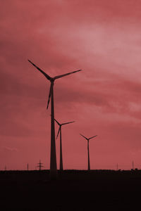 Silhouette wind turbines on field against sky during sunset