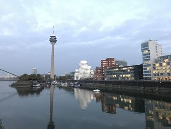 Reflection of buildings in city against cloudy sky