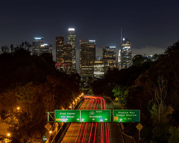 Illuminated information sign by modern buildings in city at night