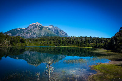 Scenic view of lake and mountains against clear blue sky