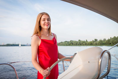Beautiful lady skipper in a long red dress holding the helm of the ship