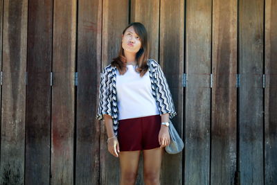 Thoughtful young woman standing against wooden fence