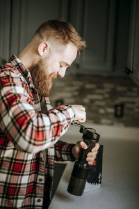 Man with beard smiles while grinding coffee in his kitchen in morning