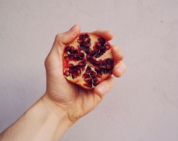 Cropped hand holding pomegranate against wall