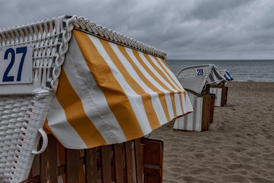Hooded chairs on beach against sky