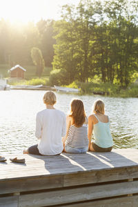 Rear view of friends sitting on pier by lake