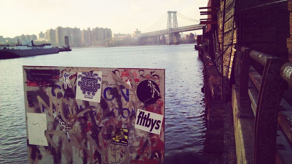 built structure, architecture, water, building exterior, city, transportation, text, river, connection, bridge - man made structure, western script, graffiti, outdoors, railing, sky, day, clear sky, no people, communication, reflection