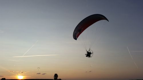 Low angle view of people paragliding against sky