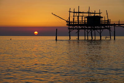 Silhouette built structure over sea against sky during sunset