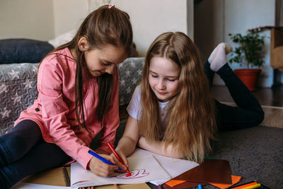 Two girls friends play at home, draw with pencils and felt-tip pens and have fun