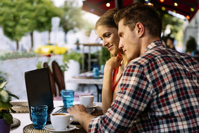 Couple watching video over laptop while sitting at sidewalk cafe