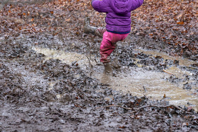 Low section of child playing in muddy puddle at land