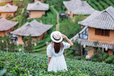 Rear view of woman wearing hat on field against building