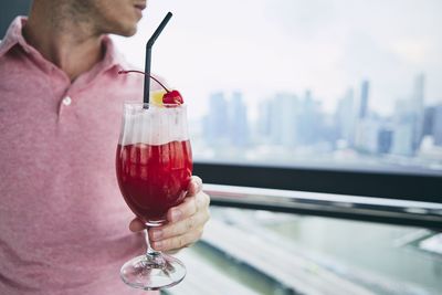 Midsection of man holding drinking glass by window in restaurant