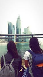 Rear view of woman on bridge over river in city against clear sky