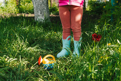 Child in rubber boots stands in the garden near a small watering can. part of the human body. 