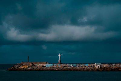 Lighthouse by sea and buildings against sky