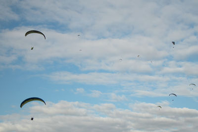 Low angle view of people paragliding against sky