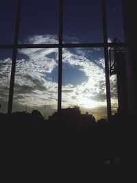 Silhouette buildings seen through window at sunset