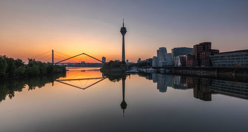 Reflection of buildings in city against sky during sunset