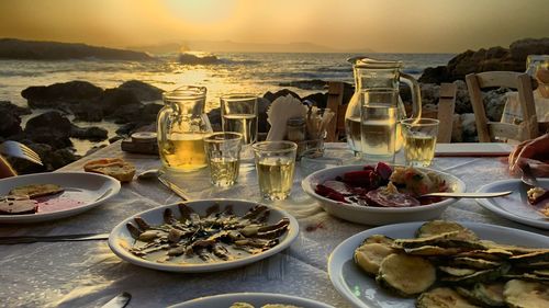Food on table at beach against sky during sunset