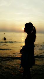 Silhouette woman standing on beach against sky during sunset