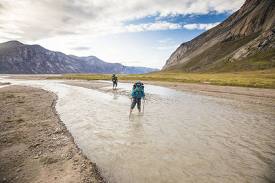 Two backpackers crossing river on baffin island.