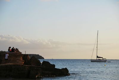 Sailboat on rocks by sea against sky