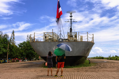 Rear view of friends standing by ship against sky