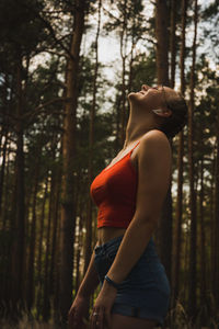 Side view of woman standing against trees in forest