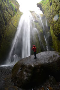 Man standing on rock against waterfall