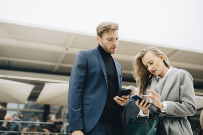 Low angle view of businesswoman using phone while standing by colleague in city