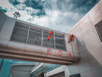 Low angle view of people working on building against sky