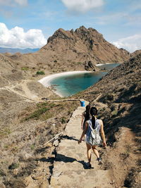 Rear view of women walking on pathway amidst mountain by sea against sky