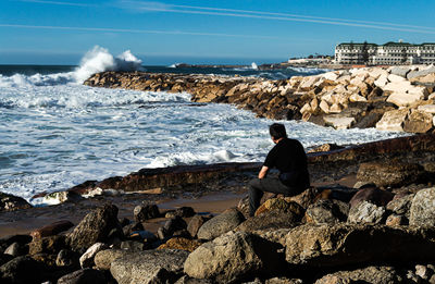 Rear view of woman sitting on rock at beach